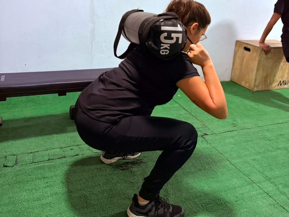 Alumna de CENIS haciendo sentadillas con una bolsa de 15 kilos